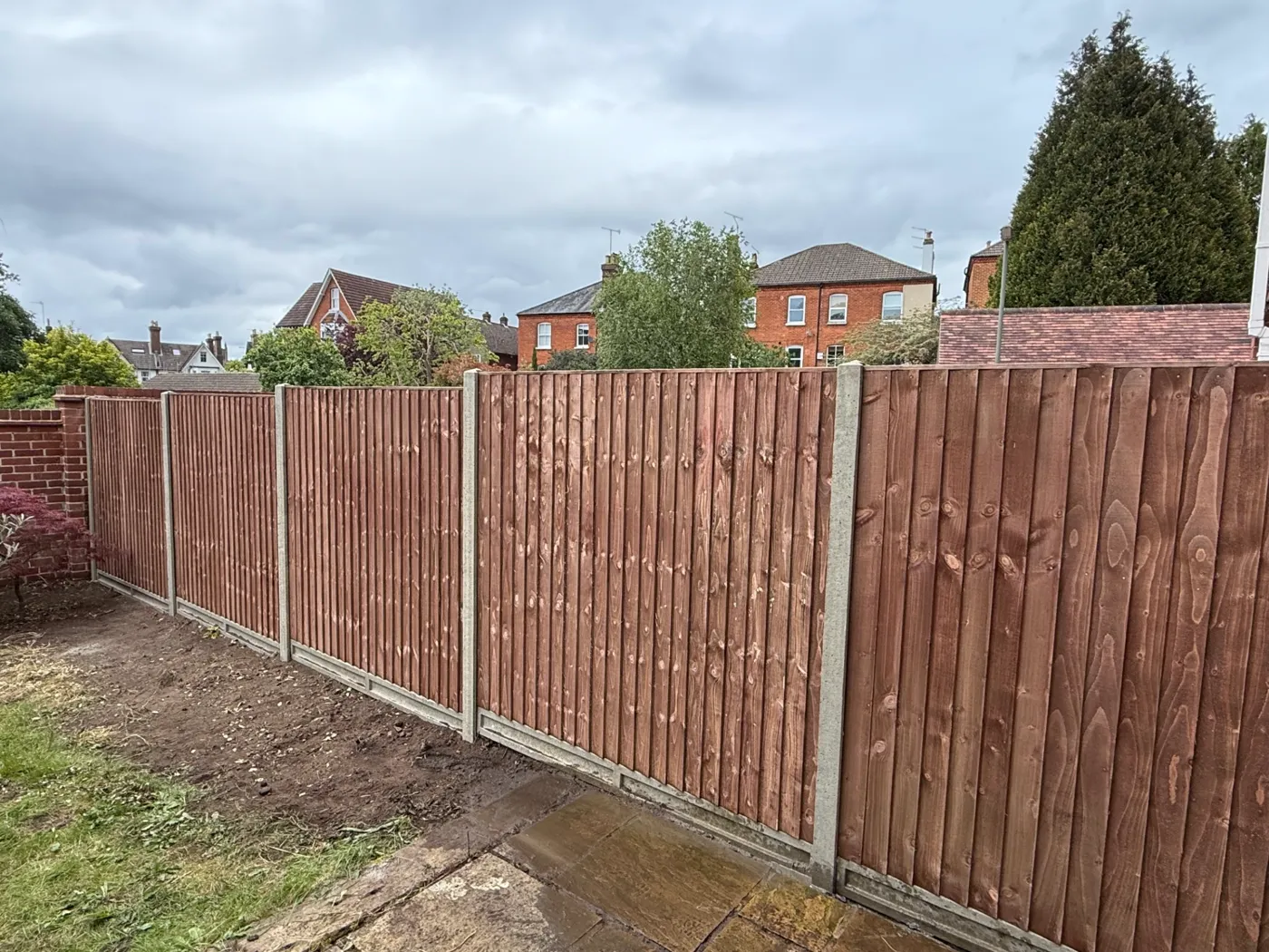 Brown stained closeboard fencing with concrete posts behind a house
